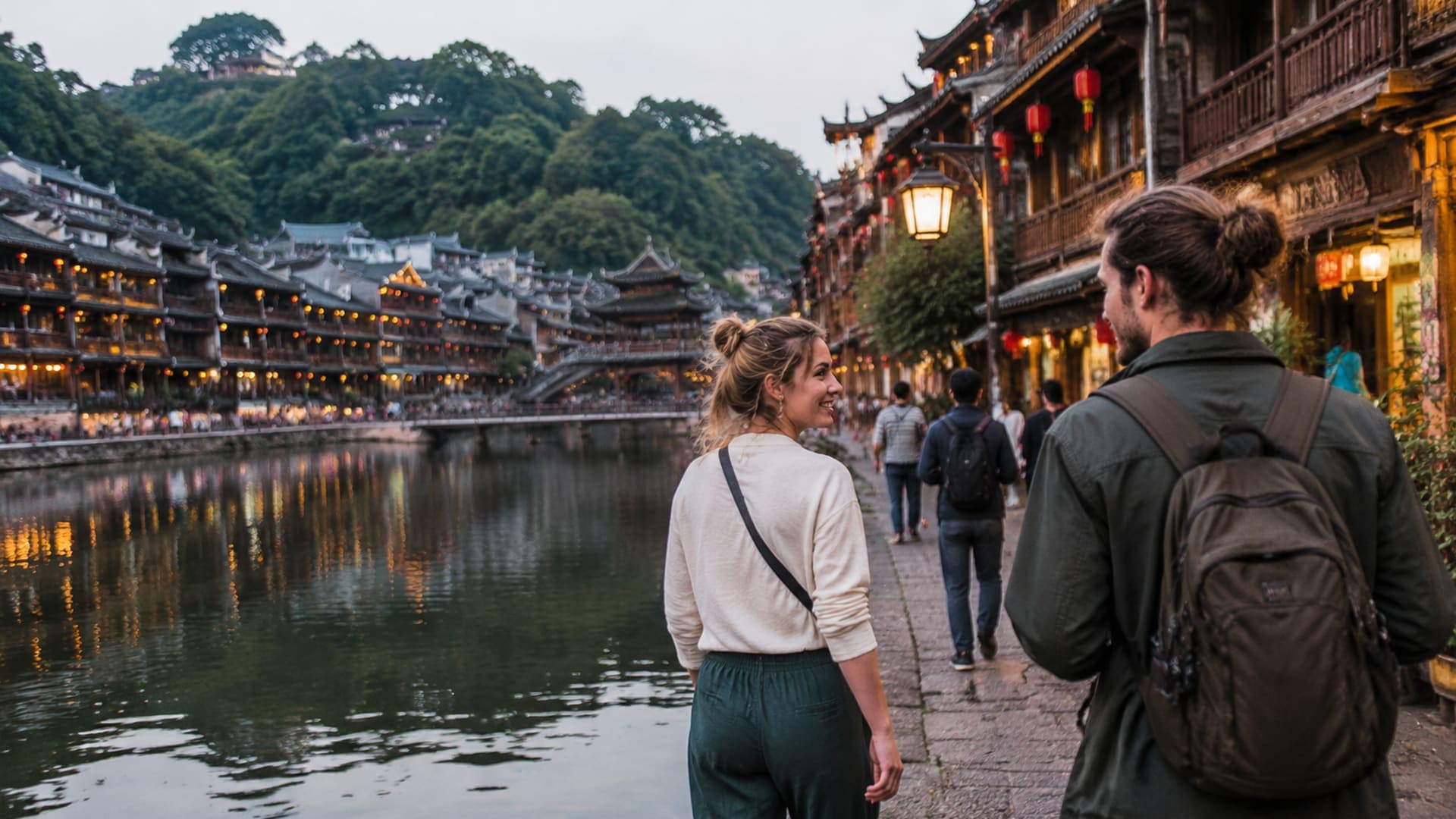 European travelers walking beside a western Hunan riverside old town at dusk