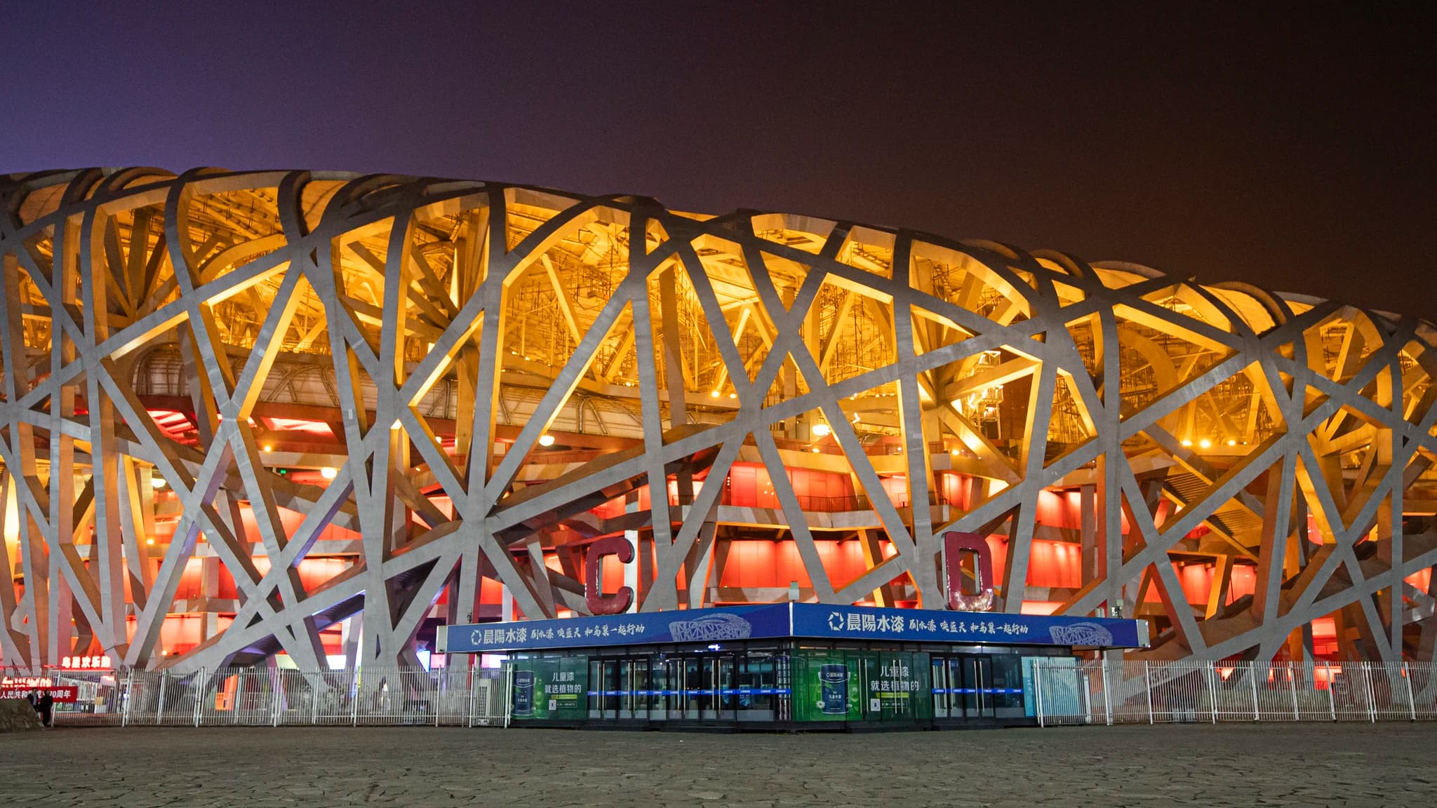 The Bird's Nest national stadium at night, its interwoven steel structure lit warm gold with red accents below